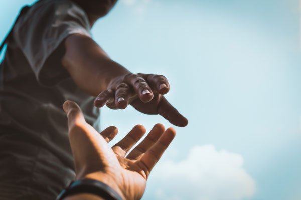 A hand reaching out to grab another hand with sky behind the subjects depicting ADHD Support